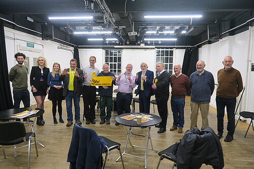 A group of 12 Exeter Lib Dems pictured launching the manifesto and campaign for the 2022 Exeter City Council elections. One of the central ones holds up a 'Liberal Democrats' banner