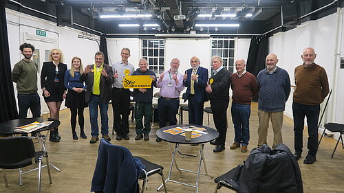 A group of 12 Exeter Lib Dems pictured launching the manifesto and campaign for the 2022 Exeter City Council elections. One of the central ones holds up a 'Liberal Democrats' banner