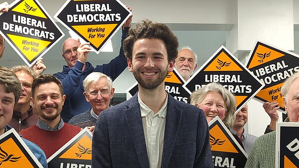 Aill Aczel in front of a crowd of Exeter Lib Dem holding Lib Dem working for you posterboards