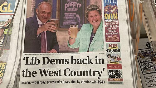 Ed Davey and Sarah Dyke say cheers with their pints on the Western Daily Press newspaper with the headline 'Lib Dems back in the West Country'. Sub-heading: 'Trend now clear says party leader Davey after by-election win.'