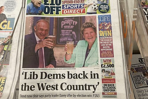 Ed Davey and Sarah Dyke say cheers with their pints on the Western Daily Press newspaper with the headline 'Lib Dems back in the West Country'. Sub-heading: 'Trend now clear says party leader Davey after by-election win.'